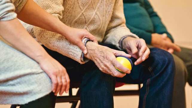 Senior man squeezing ball with female carer checking pulse