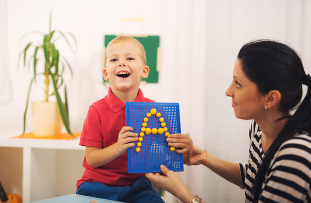 Picture1 Young boy holding up a letter A with support from Female adult