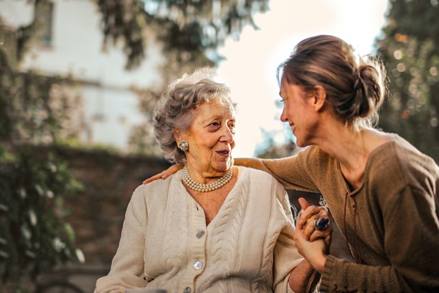 Elderly woman in cardigan, in wheelchair, speaking with a younger woman