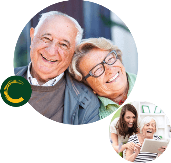 An elderly couple smiling with the woman's head on the man's shoulder and a woman assisting an older woman with the tablet, both are smiling