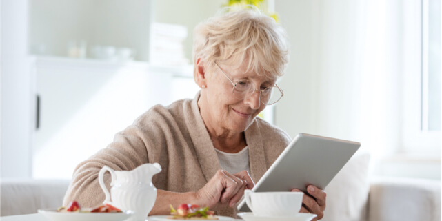 An older woman staring at her tablet while smiling