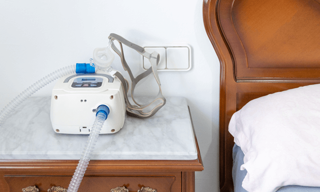 CPAP Machine with Air Hose and Head Mask on Bedside Table