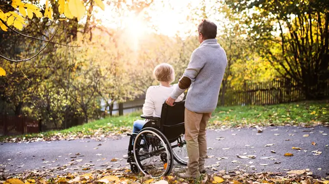 Man wheeling woman in a wheelchair at a park staring into the sunset