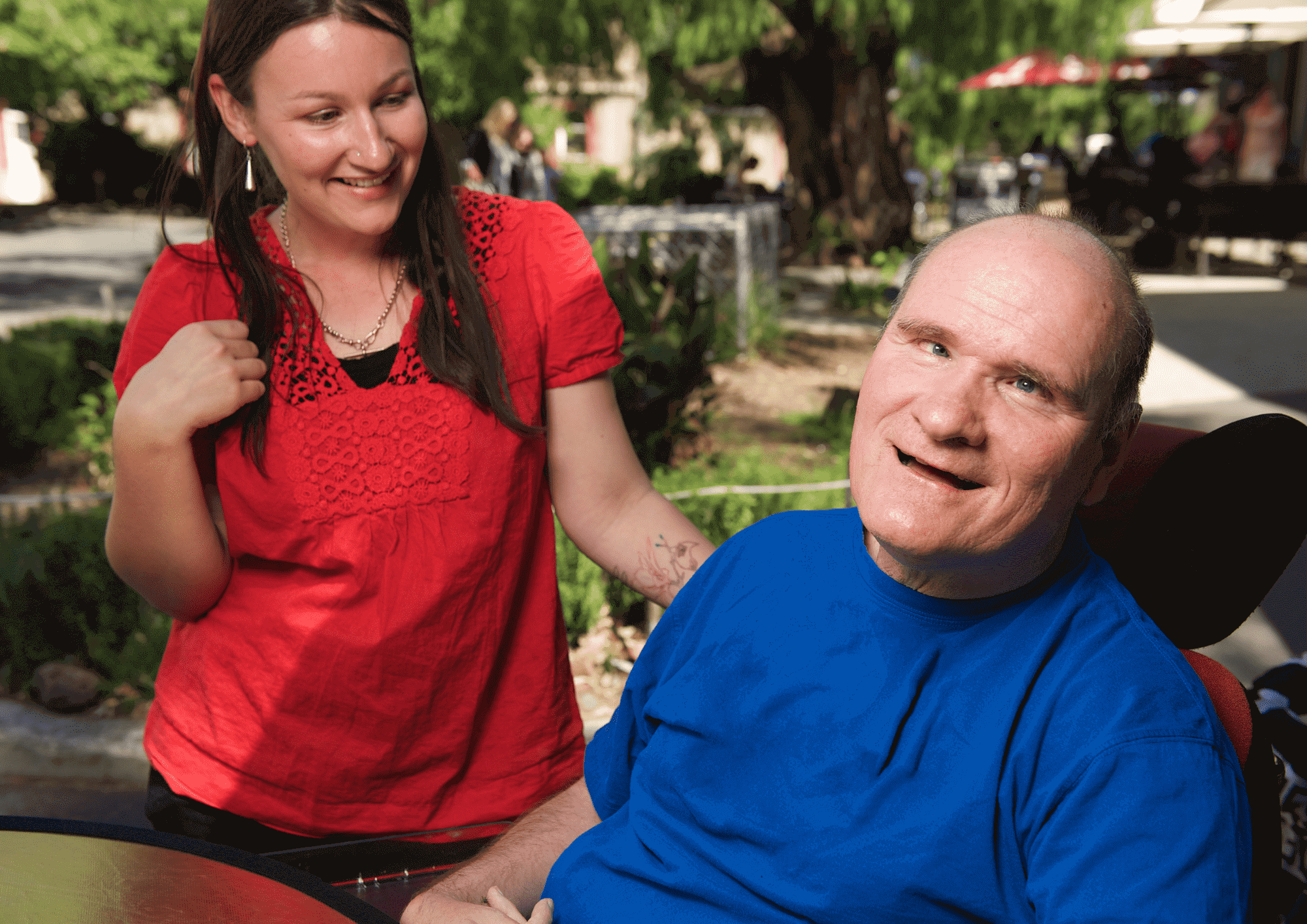 A woman stands next to and smiles at a disabled man in a wheelchair.