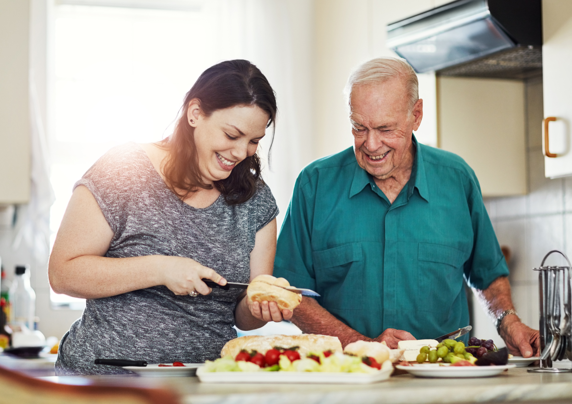 A young woman and an elderly man make sandwiches in the kitchen.