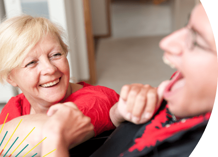 Older woman smiling and looking at a man with a disability who is laughing