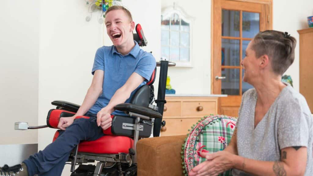 A woman stands next to and smiles at a disabled man in a wheelchair.